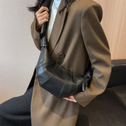 Donna con cappotto marrone indossa borsa a tracolla nera in pelle, design moderno, moda autunno inverno, accessorio elegante per outfit casual.