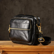 Borsa a tracolla in pelle nera con cerniere dorate, design elegante e compatto, ideale per uomo, accessorio moda versatile e di tendenza.