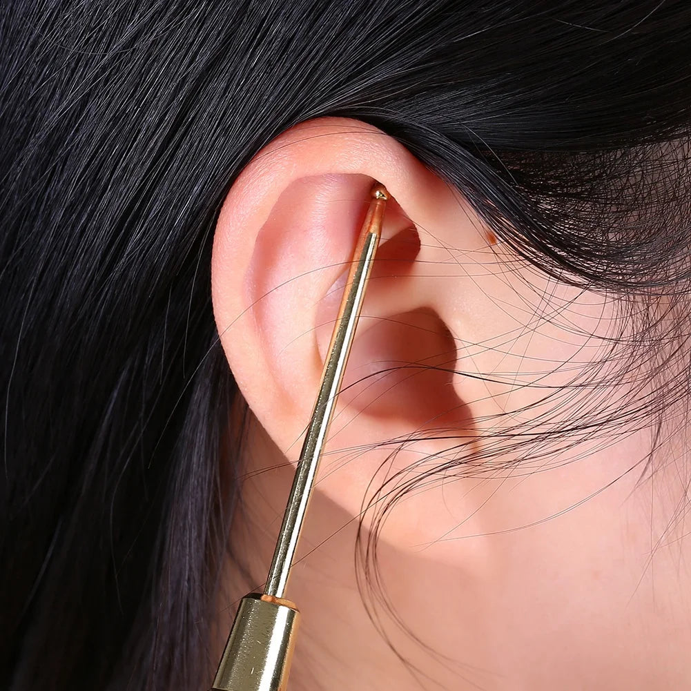 Strumento per pulizia orecchie in metallo dorato, rimozione cerume, igiene auricolare, accessorio cura personale, dettaglio su orecchio umano.