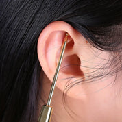 Strumento per pulizia orecchie in metallo dorato, rimozione cerume, igiene auricolare, accessorio cura personale, dettaglio su orecchio umano.