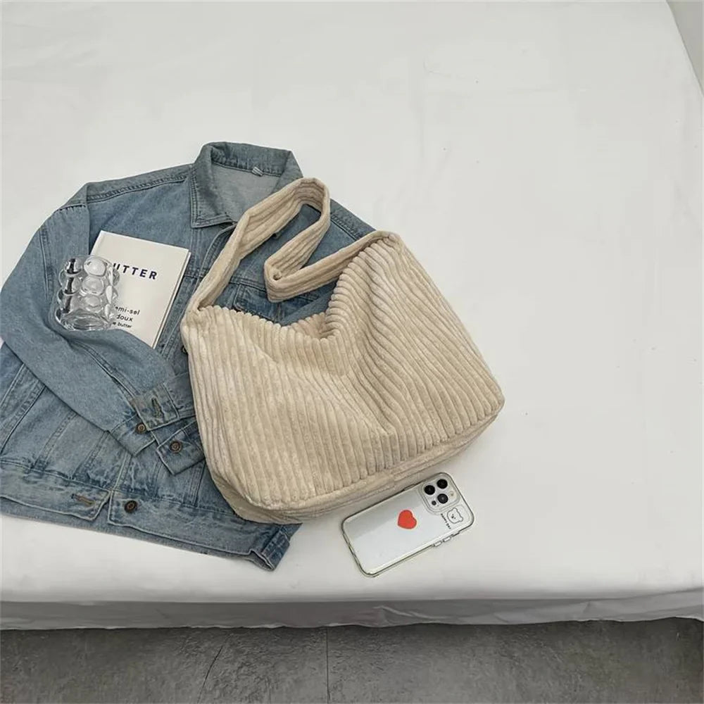 Borsa a spalla beige in velluto a coste su giacca di jeans, con libro e smartphone. Accessori moda casual, stile autunnale.
