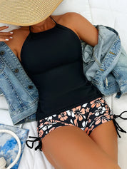 Donna in costume da bagno nero con pantaloncini floreali, giacca di jeans e cappello di paglia. Moda estiva, abbigliamento mare, stile casual.