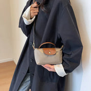 Donna con cappotto nero indossa borsa a tracolla beige e marrone, elegante e compatta, perfetta per moda autunnale. Accessorio chic e versatile.