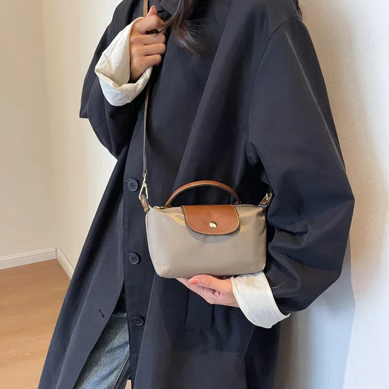 Donna con cappotto nero indossa borsa a tracolla beige e marrone, elegante e compatta, perfetta per moda autunnale. Accessorio chic e versatile.