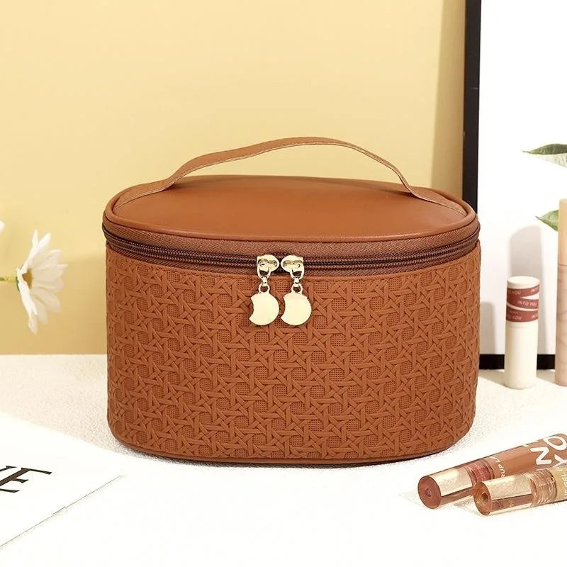 Borsa cosmetica marrone in pelle sintetica con motivo intrecciato, cerniera dorata e manico superiore. Accessorio elegante per trucco e viaggio.