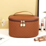 Borsa cosmetica marrone in pelle sintetica con motivo intrecciato, cerniera dorata e manico superiore. Accessorio elegante per trucco e viaggio.