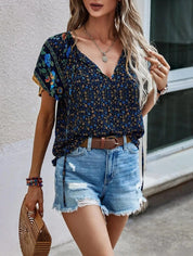 Donna con top floreale blu e shorts di jeans strappati, accessoriata con borsa in legno e braccialetti colorati. Moda estiva casual femminile.
