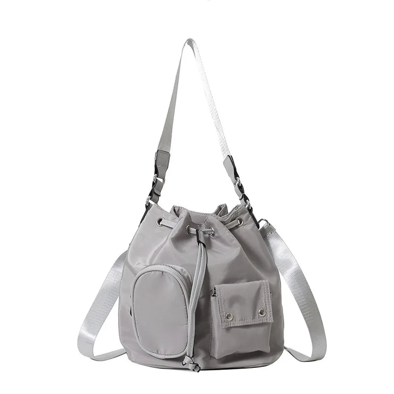 Borsa a secchiello grigia in nylon con tracolla regolabile, tasca frontale con zip e chiusura a coulisse. Design moderno e funzionale.