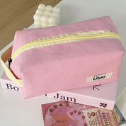 Astuccio rosa in tessuto con cerniera gialla, marchio "ütoo", su libri e decorazioni. Accessorio moda, organizzazione, scuola, viaggio.