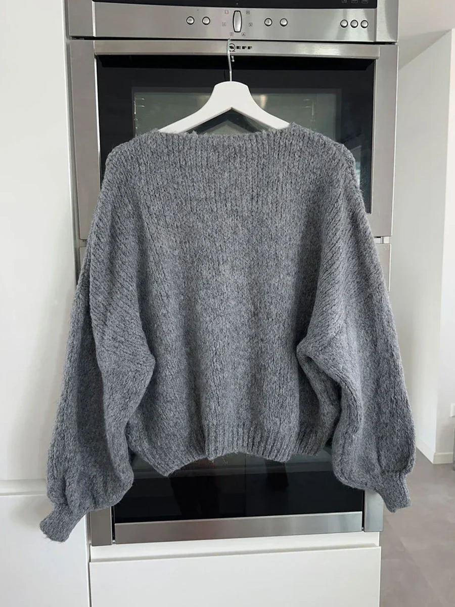 Maglione grigio in lana, oversize, appeso su gruccia bianca davanti a forno moderno. Morbido, caldo, ideale per l'inverno.
