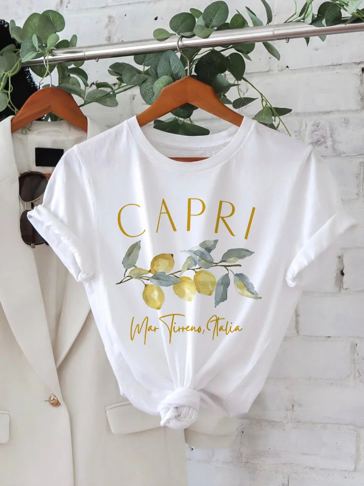 Maglietta bianca con stampa "Capri" e limoni, appesa su gruccia. Design estivo, moda casual, abbigliamento donna, ispirazione italiana.