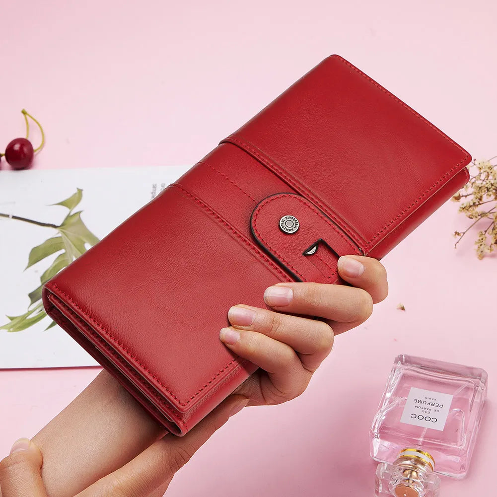 Portafoglio rosso in pelle elegante, chiusura a bottone, tenuto in mano su sfondo rosa. Accessorio moda donna, design raffinato.