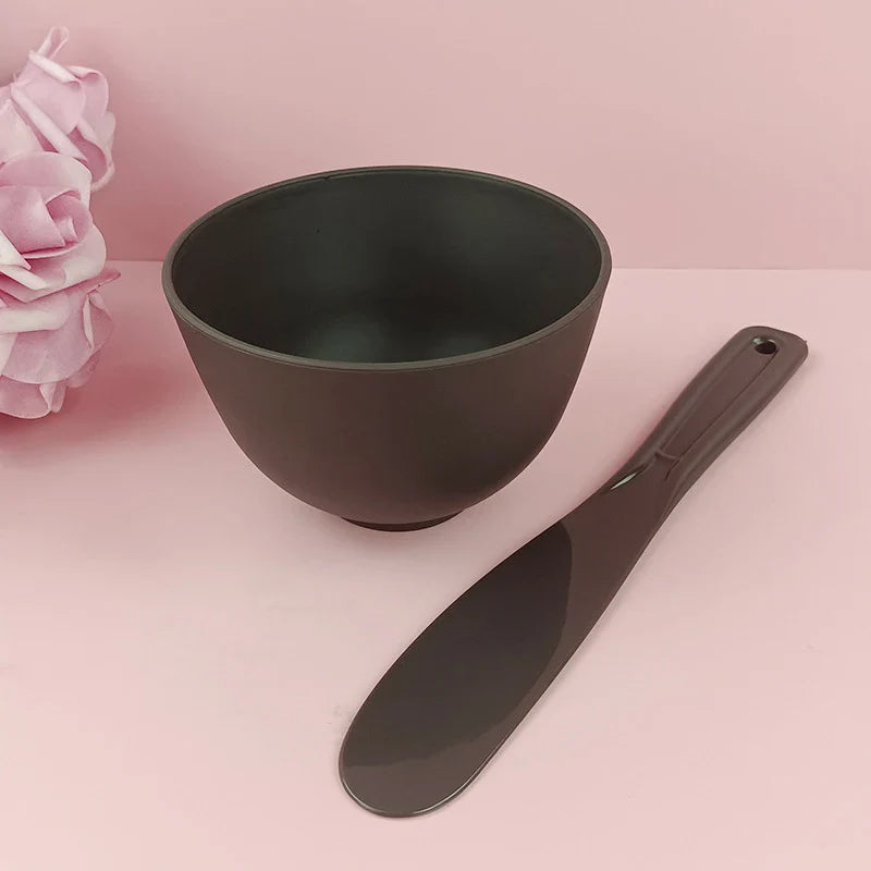 Ciotola nera opaca con spatola su sfondo rosa, ideale per cucina moderna. Accessori eleganti per preparazioni culinarie.