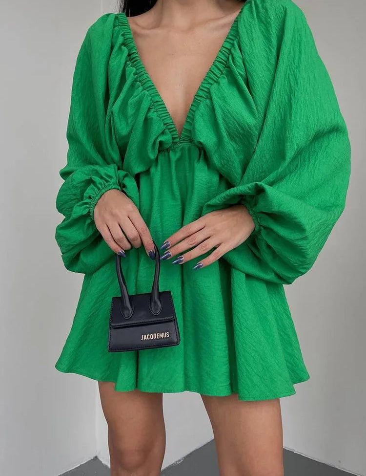 Donna in abito verde con scollo profondo e maniche ampie, tiene una mini borsa nera Jacquemus. Moda elegante, abbigliamento femminile trendy.