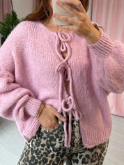 Cardigan rosa in maglia con lacci decorativi, indossato da una donna. Moda autunnale, abbigliamento casual, stile femminile.