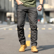 Pantaloni cargo uomo grigi, tasche multiple, indossati con stivali gialli su strada urbana. Abbigliamento casual maschile, moda outdoor.