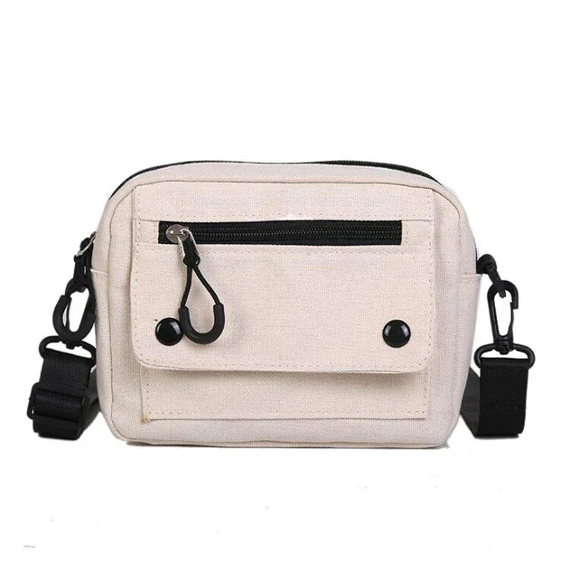 Borsa a tracolla in tela beige con tasca frontale con zip, chiusura a bottone e tracolla regolabile nera. Accessorio moda unisex casual.