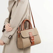 Borsa a tracolla beige in pelle con dettagli marroni, design elegante, indossata da una persona con cappotto beige. Accessorio moda donna.