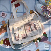 Borsa a tracolla beige con tasche multiple e spille decorative su coperta colorata, accanto a scarpe sportive multicolore. Accessori moda casual.