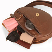 Borsa a tracolla in pelle marrone con cerniera aperta, contenente occhiali da sole, smartphone, rossetto e fazzoletto rosa. Accessori moda donna.