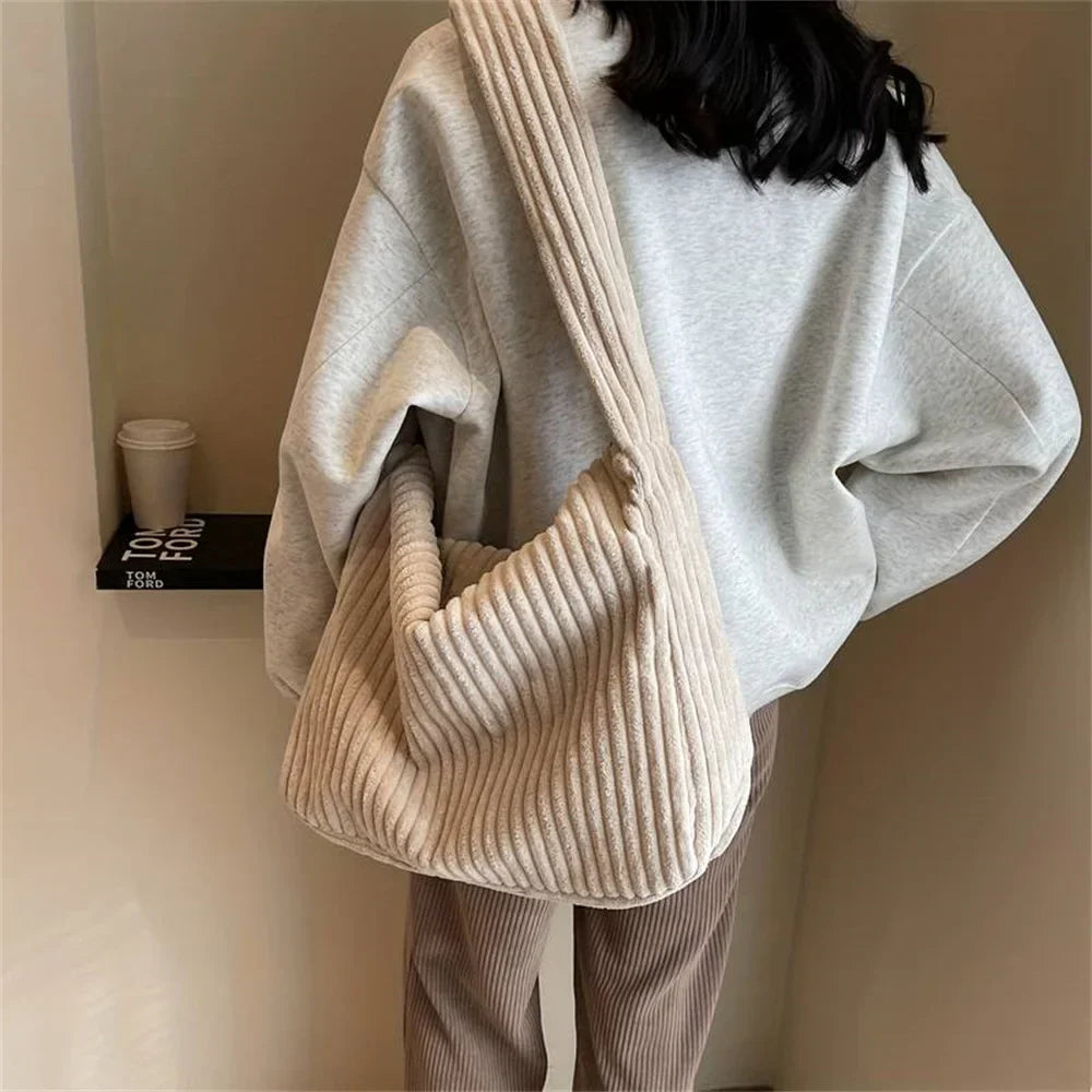 Donna con borsa a tracolla beige in tessuto a coste, indossa felpa grigia e pantaloni marroni. Moda casual autunnale, accessori femminili eleganti.