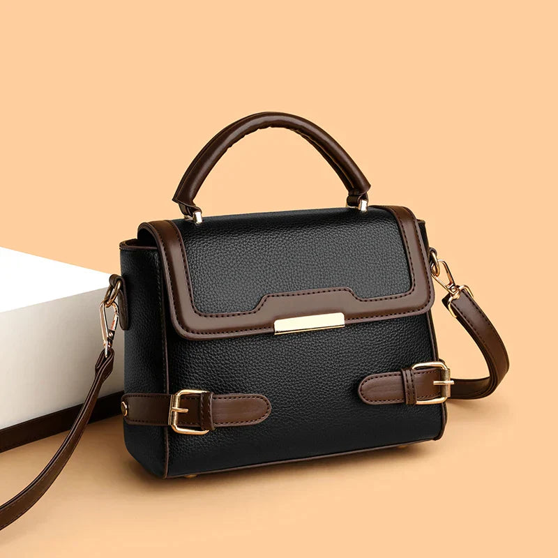 Borsa a tracolla in pelle nera e marrone con manico superiore, fibbie decorative e chiusura dorata. Elegante accessorio moda donna.