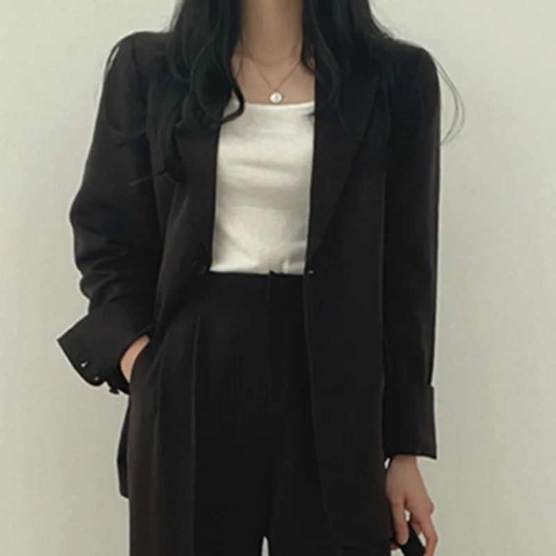 Donna in abito elegante nero, giacca e pantaloni, con top bianco. Moda femminile, abbigliamento formale, stile business casual.