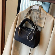 Borsa a tracolla nera in nylon con manico arricciato, appesa a un cappotto beige. Design elegante, moda donna, accessorio versatile.