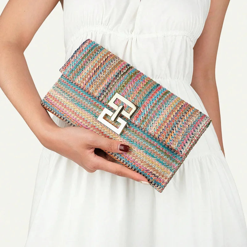 Donna con abito bianco tiene una pochette multicolore intrecciata, chiusura metallica geometrica. Elegante borsa a mano estiva.