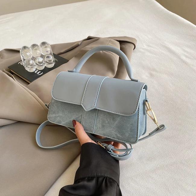 Borsa a tracolla in pelle blu chiaro su letto beige, design elegante, chiusura a patta, manico superiore, ideale per moda femminile e accessori di lusso.