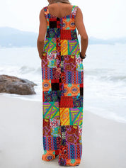 Donna in spiaggia con tuta lunga patchwork colorata, design geometrico e floreale, moda estiva, abbigliamento casual, mare sullo sfondo.