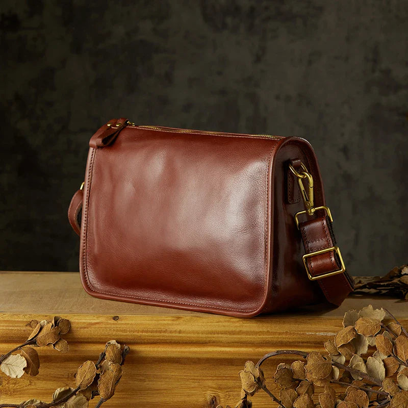 Borsa a tracolla in pelle marrone su tavolo di legno, design elegante e classico, accessorio moda donna, chiusura con fibbia dorata.