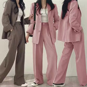 Tre donne in abiti eleganti: due completi rosa e uno marrone, con pantaloni larghi e giacche, su sfondo bianco. Moda femminile, abbigliamento formale.