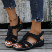 Sandali neri con zeppa, decorati con fiori, indossati con jeans strappati e cavigliera dorata. Scarpe estive eleganti e comode per donna.