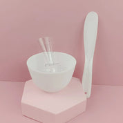 Set per maschera viso: ciotola bianca, spatola e misurino su sfondo rosa. Accessori per skincare, strumenti bellezza, cura del viso.