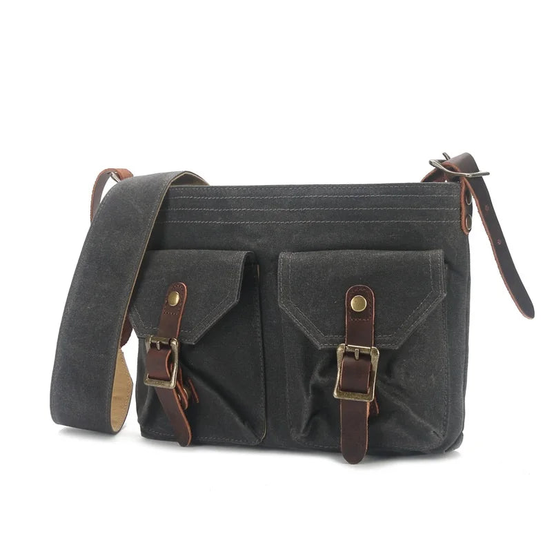 Borsa a tracolla in tela cerata grigia con doppie tasche frontali e fibbie in pelle marrone, stile vintage, ideale per uomo e donna.