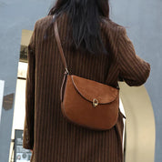 Donna con cappotto marrone a righe indossa borsa a tracolla in pelle marrone, design elegante, chiusura a gancio, moda autunnale, accessorio femminile.