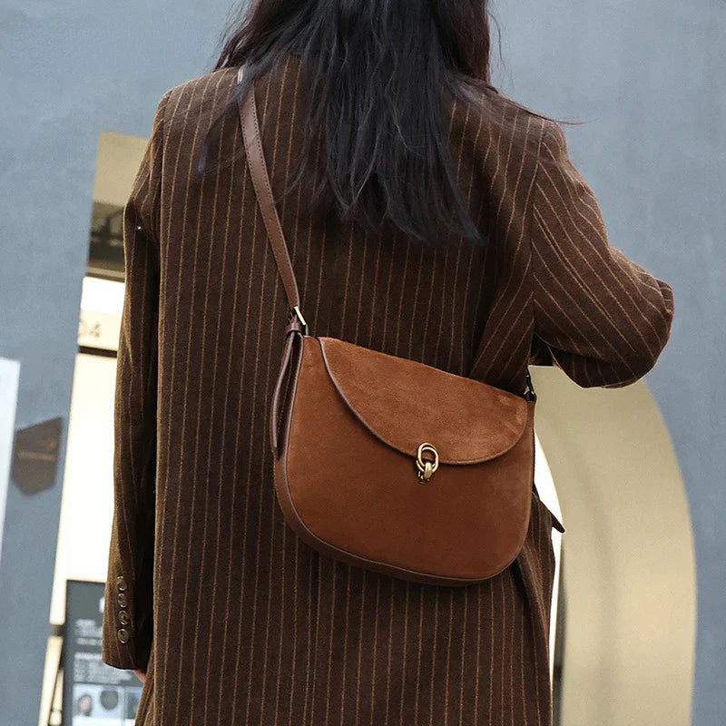Donna con cappotto marrone a righe indossa borsa a tracolla in pelle marrone, design elegante, chiusura a gancio, moda autunnale, accessorio femminile.