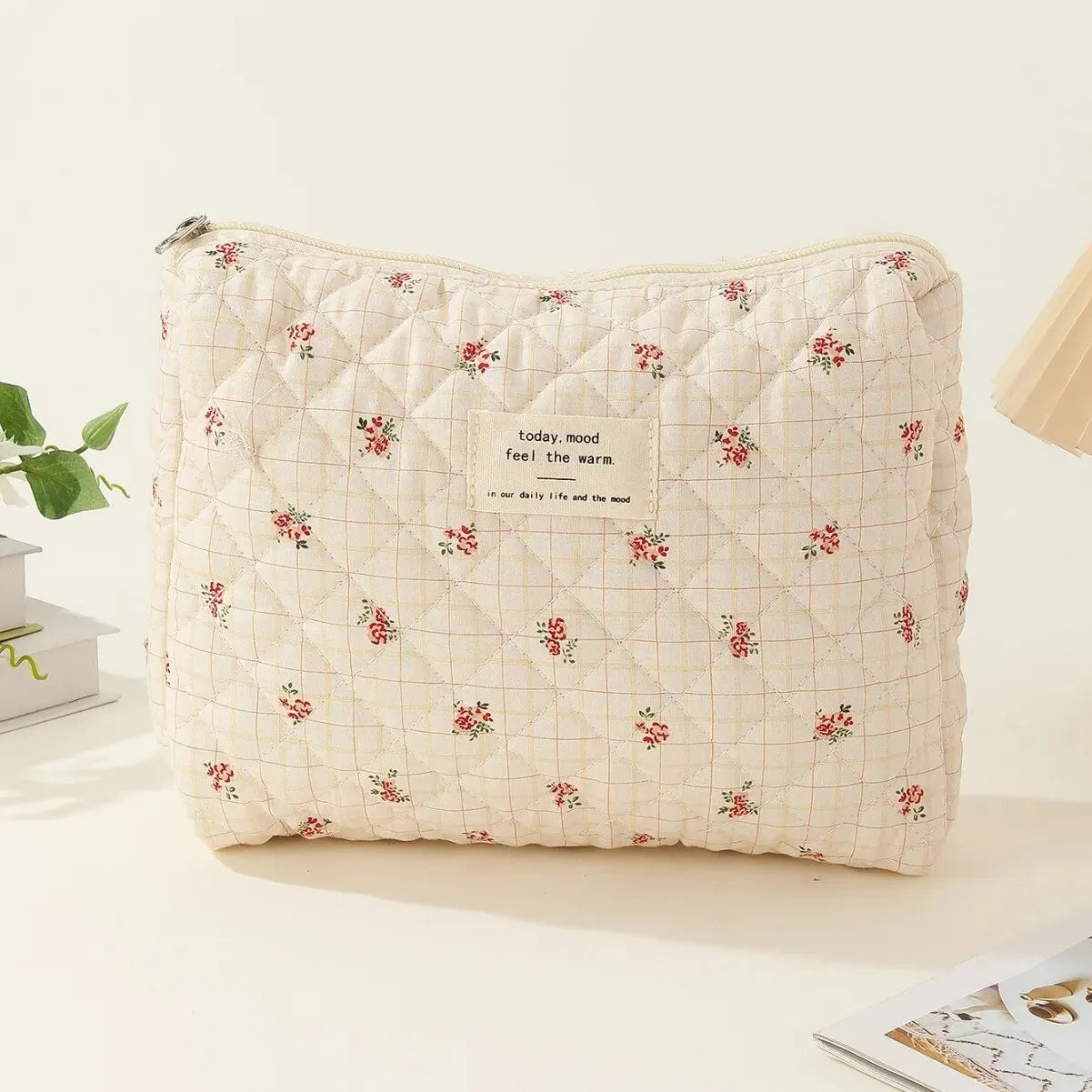 Borsa trapuntata beige con motivo floreale rosso, etichetta "today, mood feel the warm", su sfondo chiaro. Accessorio moda elegante e pratico.