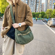 Giovane con camicia marrone e borsa a tracolla verde in strada urbana. Moda casual, accessori trendy, look estivo.