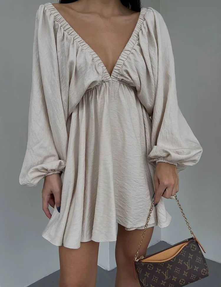 Abito corto beige con scollo a V profondo e maniche lunghe a sbuffo, borsa a tracolla marrone con logo. Elegante moda femminile autunnale.