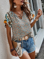 Donna con top floreale e shorts di jeans, accessoriata con cintura beige, borsa con frange e gioielli boho-chic. Look estivo casual e alla moda.