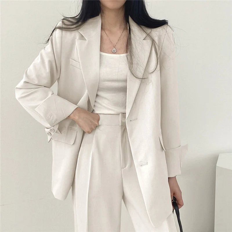 Donna in elegante completo bianco, giacca e pantaloni, moda minimalista, abbigliamento formale, stile contemporaneo, sfondo neutro.