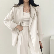 Donna in elegante completo bianco, giacca e pantaloni, moda minimalista, abbigliamento formale, stile contemporaneo, sfondo neutro.