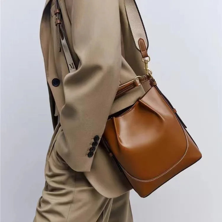 Borsa a tracolla in pelle marrone, design elegante, indossata con abito beige. Accessorio moda uomo, stile casual chic, alta qualità.