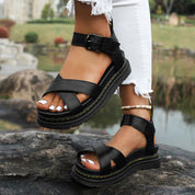 Sandali neri in pelle con cinturino alla caviglia, suola spessa e dettagli cuciti, indossati con jeans bianchi strappati. Scarpe estive eleganti.