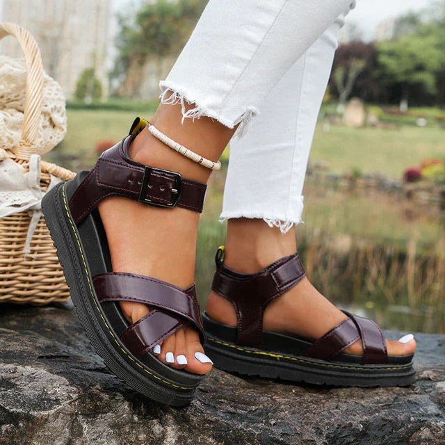 Sandali donna in pelle marrone con cinturino regolabile, suola spessa nera, indossati con jeans bianchi strappati. Scarpe estive eleganti e comode.