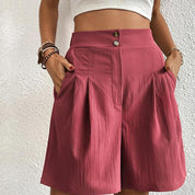 Shorts rosa a vita alta con pieghe, bottoni decorativi e tasche laterali. Moda estiva donna, abbigliamento casual elegante.