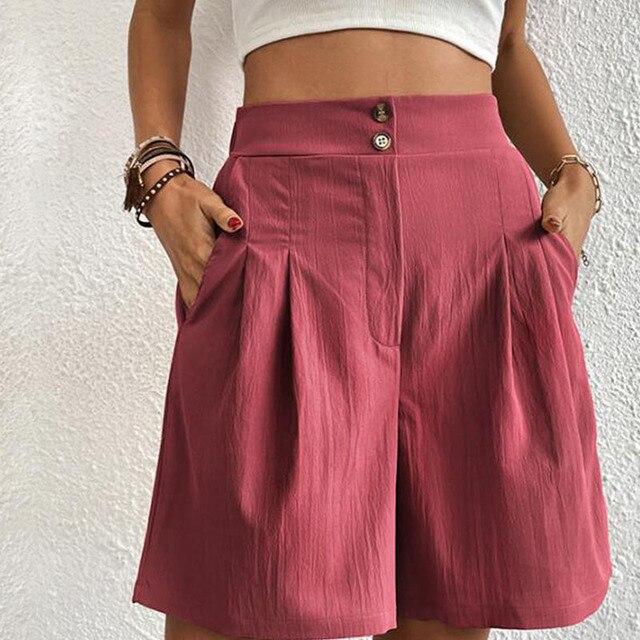 Shorts rosa a vita alta con pieghe, bottoni decorativi e tasche laterali. Moda estiva donna, abbigliamento casual elegante.