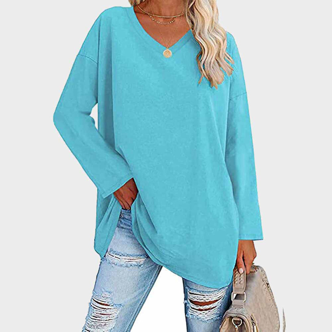 Donna con maglia oversize azzurra, scollo a V, abbinata a jeans strappati e borsa beige. Moda casual femminile, abbigliamento autunnale.